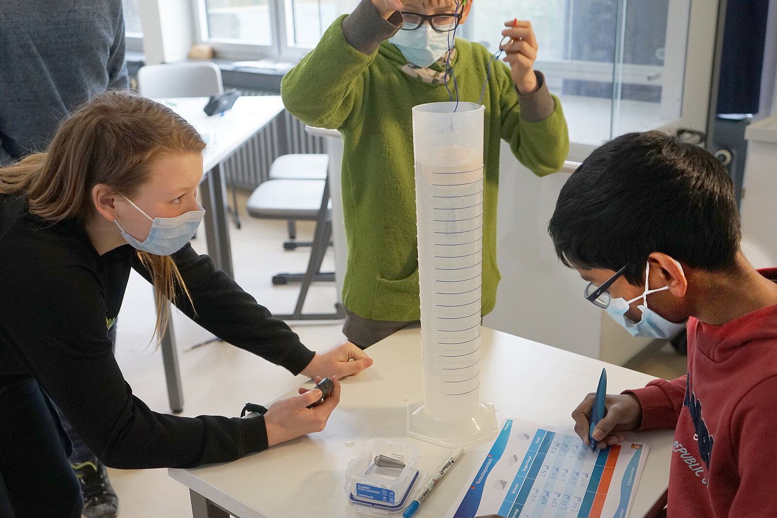 Schülerinnen und Schüler führen eine Messung in einem Messzylinder durch.