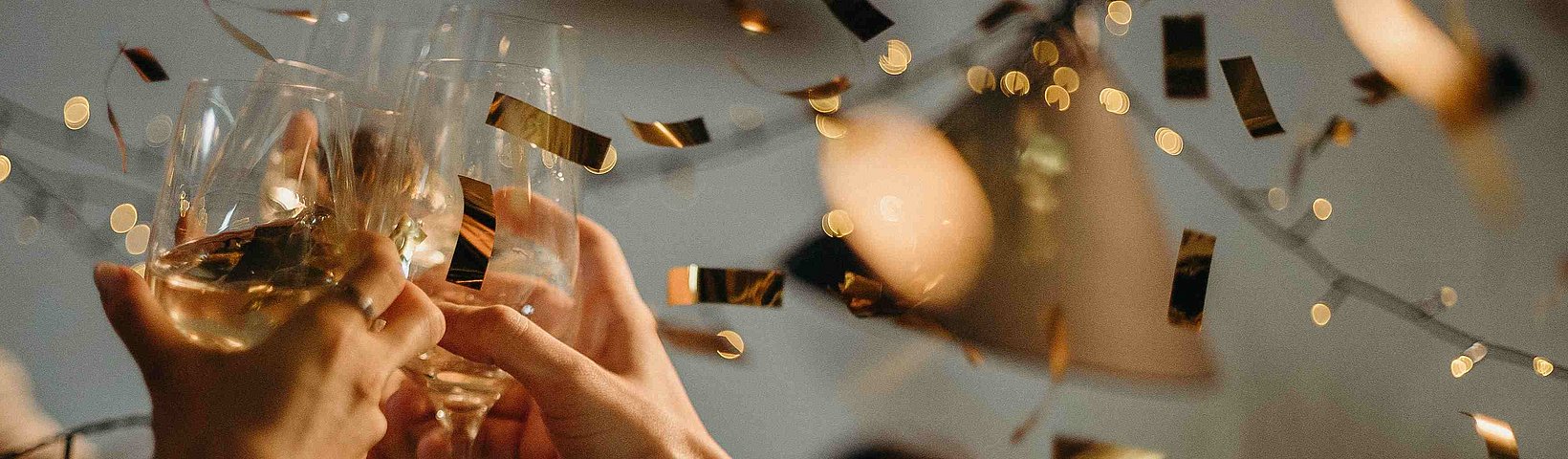Gläser in Händen, gemeinsam anstoßend, mit Konfetti 