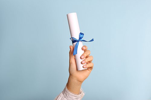 Student hält gerolltes Diplom mit Band auf hellblauem Hintergrund, Nahaufnahme