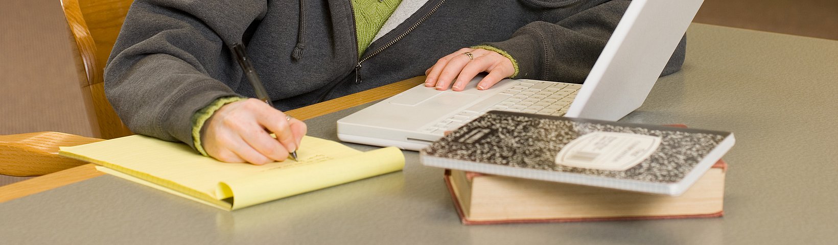 Frau am Tisch mit Labtop und Papier sitzend und schreibend 