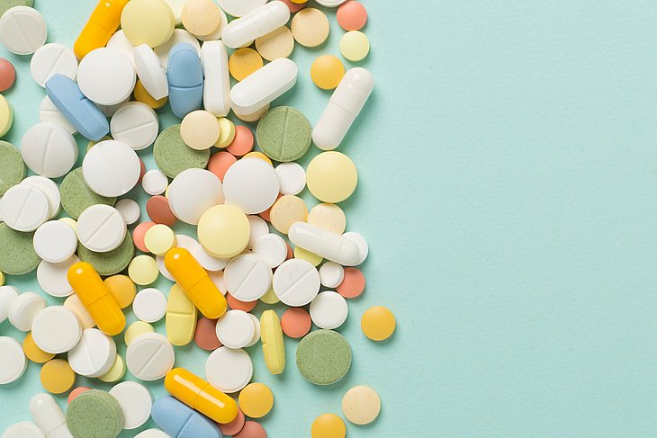 Verschiedene Medikamente in Form von Tabletten und Kapseln vor einem farbigen Hintergrund.