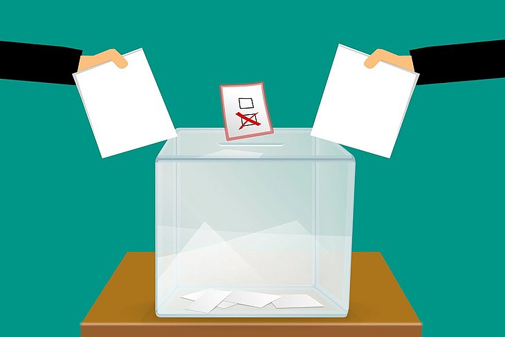 Grafik, die zwei Arme zeigt, die Stimmzettel in eine Wahlurne werfen.