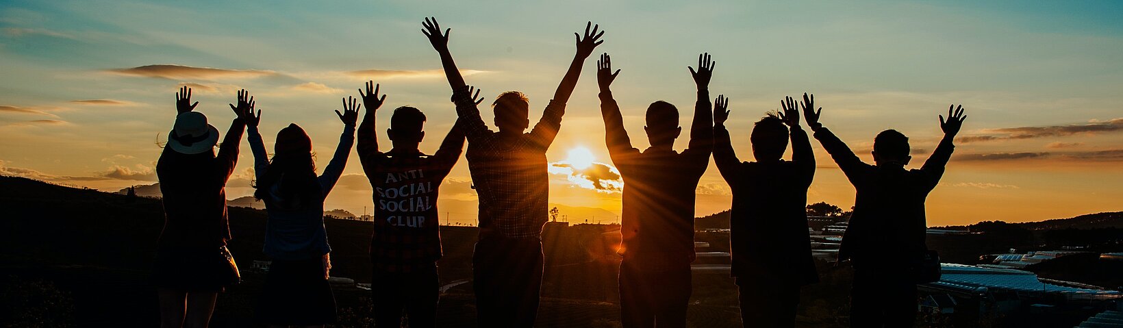 Sieben Menschen stehen jubelnd vor einem Sonnenuntergang