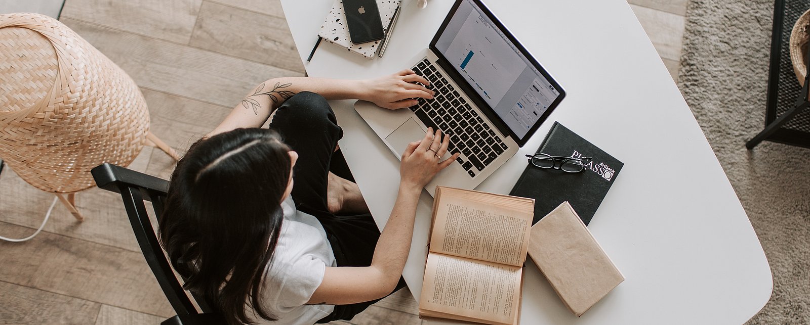 Pictured is a woman at her workplace with a notebook and various work materials