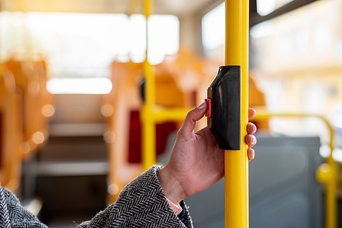 Junge Frau drückt im Bus die Taste für die Haltestellenanforderung.