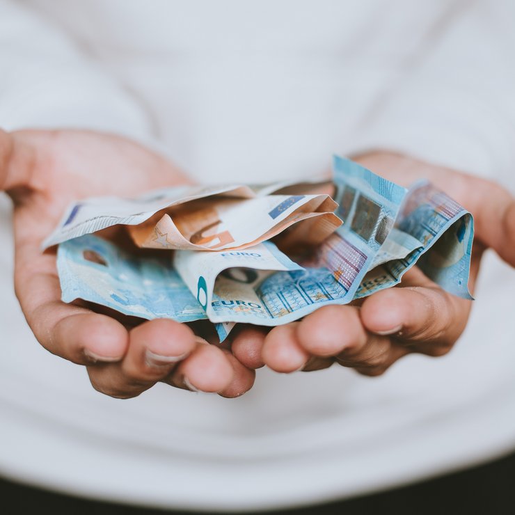 Zwei Hände halten Geld und strecken es dem Betrachtenden entgegen.