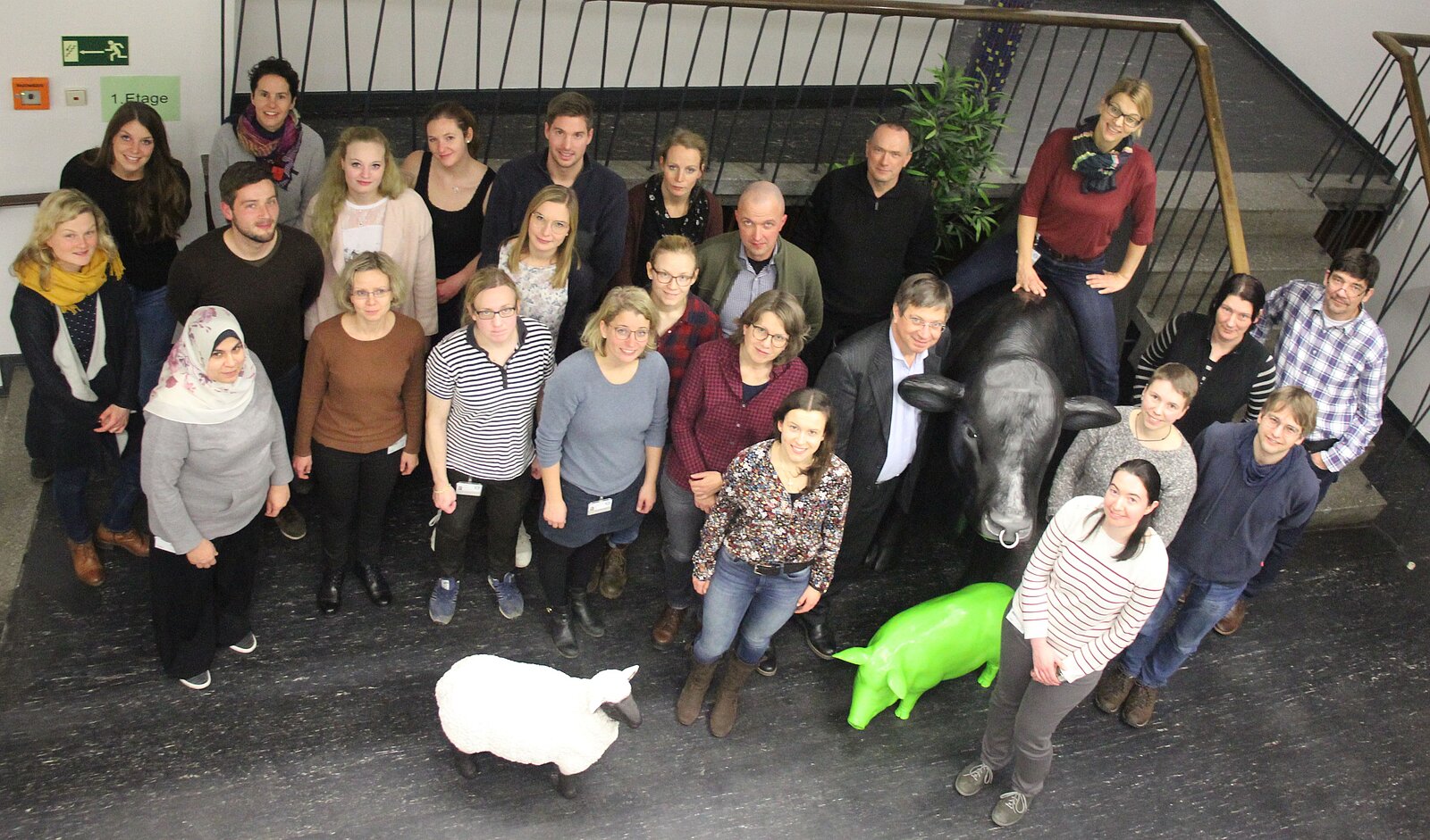 Foto: Einige Mitarbeitende des Instituts für Tierhygiene, Tierschutz und Nutztierethologie im Eingangsbereich des Instituts. Ein schwarzes Kunststoffrind in Originalgröße, ein grünes Kunststoffschwein und ein weiß-schwarzes Kunststoffschaf.