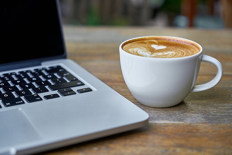 Laptop und Kaffeetasse stehen nebeneinander auf dem Tisch